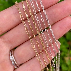 May include: Five different gold and silver chains of varying lengths and styles. The chains are arranged in a fan shape on a hand.