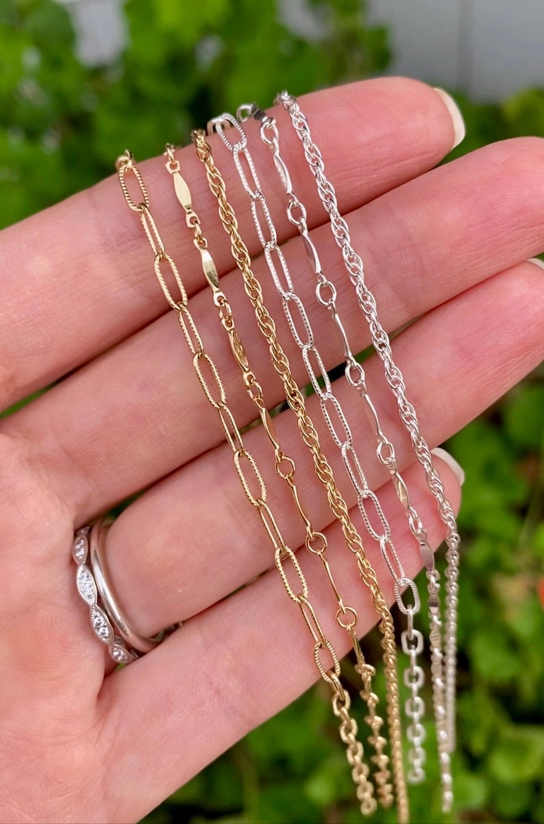May include: Five different gold and silver chains of varying lengths and styles. The chains are arranged in a fan shape on a hand.
