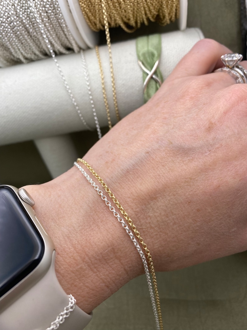 May include: Two silver and gold chains on a person's wrist. The chains are delicate and have a simple design.