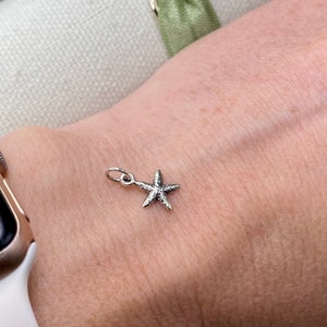 May include: A silver starfish charm on a wrist.