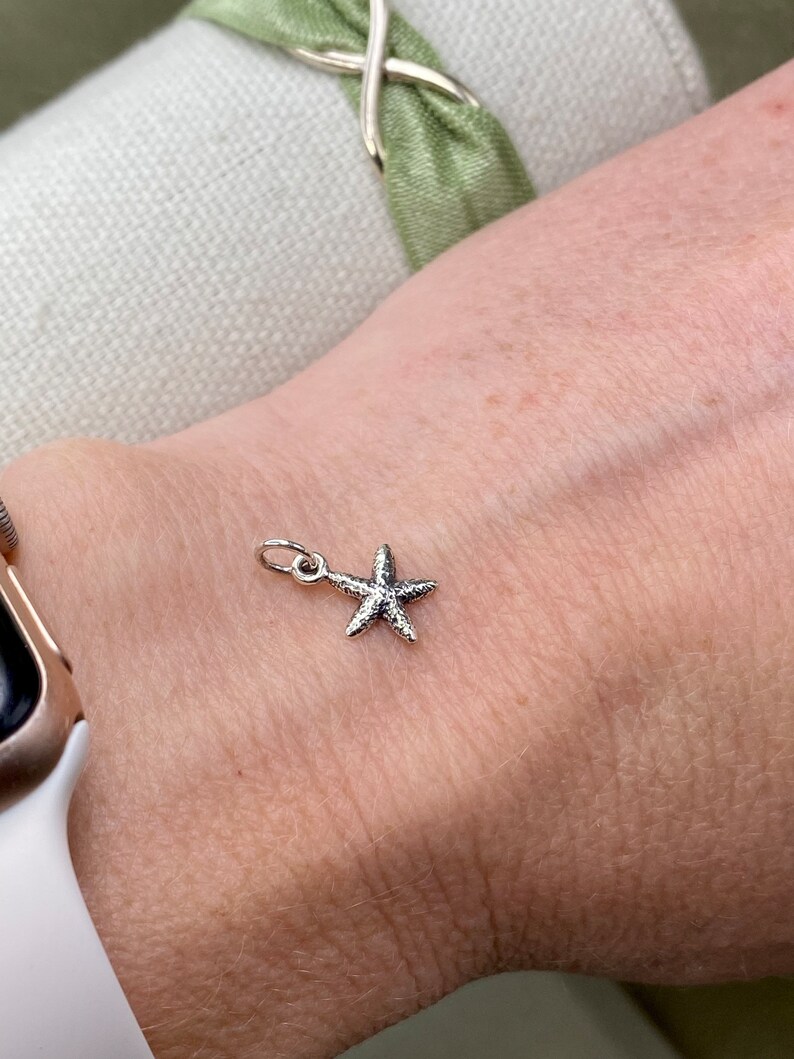 May include: A silver starfish charm on a wrist.