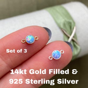 May include: Set of three opal connector charms, one in 14kt gold filled and two in 925 sterling silver. Each charm features a round opal gemstone with a light blue and white iridescent color.