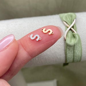 Pode incluir: Dois pingentes de metal em forma da letra "S". Um pingente &eacute; dourado e o outro &eacute; prateado.