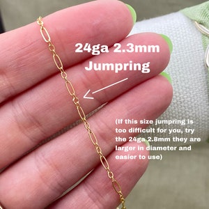 May include: Close-up of a gold-colored chain with oval links. The text overlay reads "24ga 2.3mm Jumpring". The image is of a jewelry component, likely for crafting or jewelry making. The chain is held between fingers.