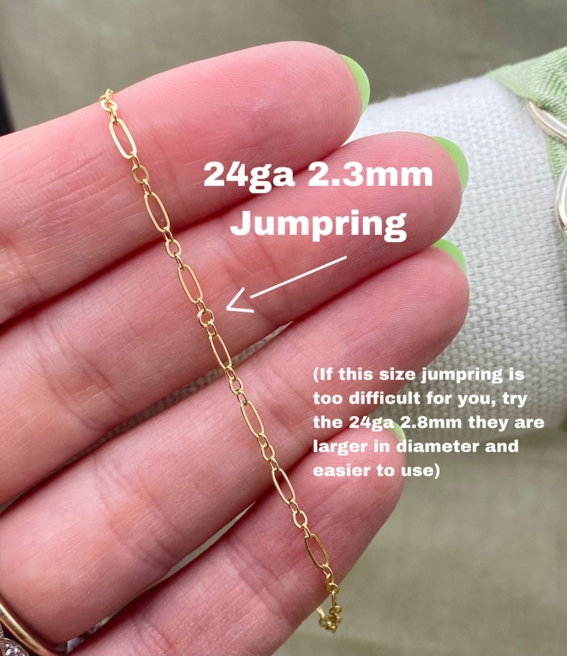 May include: Close-up of a gold-colored chain with oval links. The text overlay reads "24ga 2.3mm Jumpring". The image is of a jewelry component, likely for crafting or jewelry making. The chain is held between fingers.