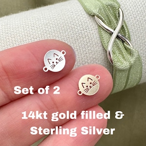 May include: Set of two cat charm connectors, one in sterling silver and one in 14kt gold filled.  The charms are round and feature a simple cat face design.