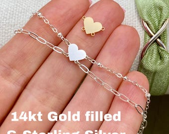 May include: A silver chain bracelet featuring a central heart charm, accompanied by a separate gold heart charm component. The text 14kt Gold filled & Sterling Silver is overlaid on the image, highlighting the metal composition of the jewelry.