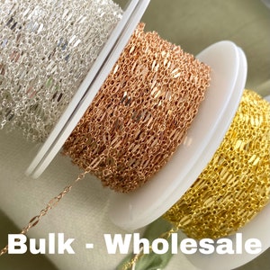 May include: Three spools of chain, one silver, one rose gold, and one gold. The chain is a flat, oval link style. The spools are labeled "Bulk - Wholesale".