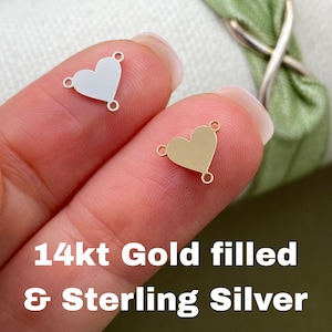May include: Two small heart-shaped jewelry connectors, one in silver-tone and one in gold-tone, each featuring two tiny circular loops on the sides for attachment. The text 14kt Gold filled & Sterling Silver is displayed at the bottom.
