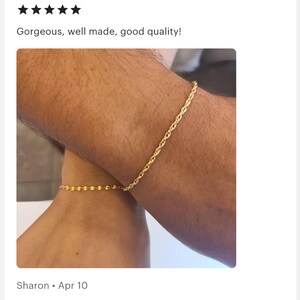 May include: Two gold chain bracelets on a person's wrists. The bracelet on the left wrist is a delicate chain, while the bracelet on the right wrist is a thicker rope chain.