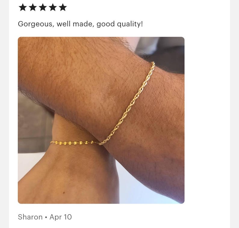 May include: Two gold chain bracelets on a person's wrists. The bracelet on the left wrist is a delicate chain, while the bracelet on the right wrist is a thicker rope chain.