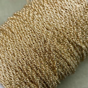 May include: A close-up of a gold-coloured chain, wound into a coil. The chain is made of small, linked loops, creating a delicate and intricate pattern.