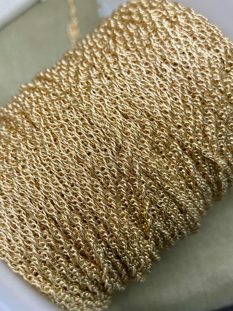 May include: A close-up of a gold-coloured chain, wound into a coil. The chain is made of small, linked loops, creating a delicate and intricate pattern.