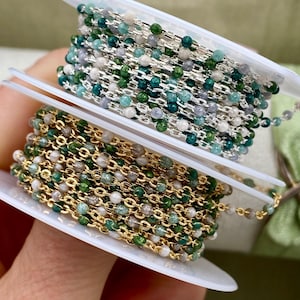 May include: Two spools of beaded chain, one with silver-toned metal links and the other with gold-toned metal links. Both chains feature small, round, multi-colored beads in shades of green, white, and grey interspersed along the metal links.