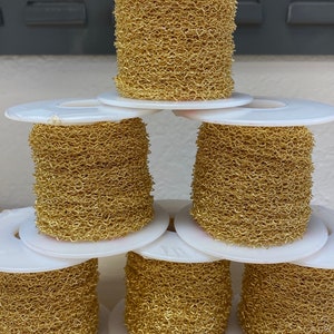 May include: Six spools of gold-colored chain link, each wound around a white plastic spool. The spools are stacked in a pyramid shape.