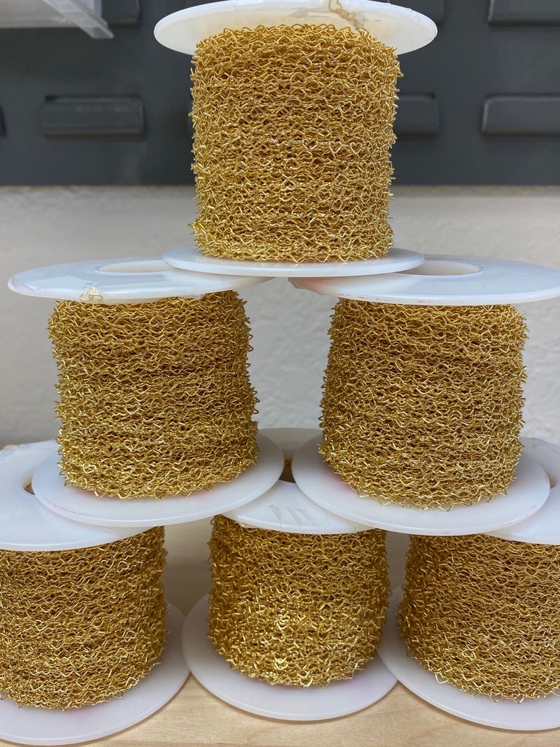 May include: Six spools of gold-colored chain link, each wound around a white plastic spool. The spools are stacked in a pyramid shape.