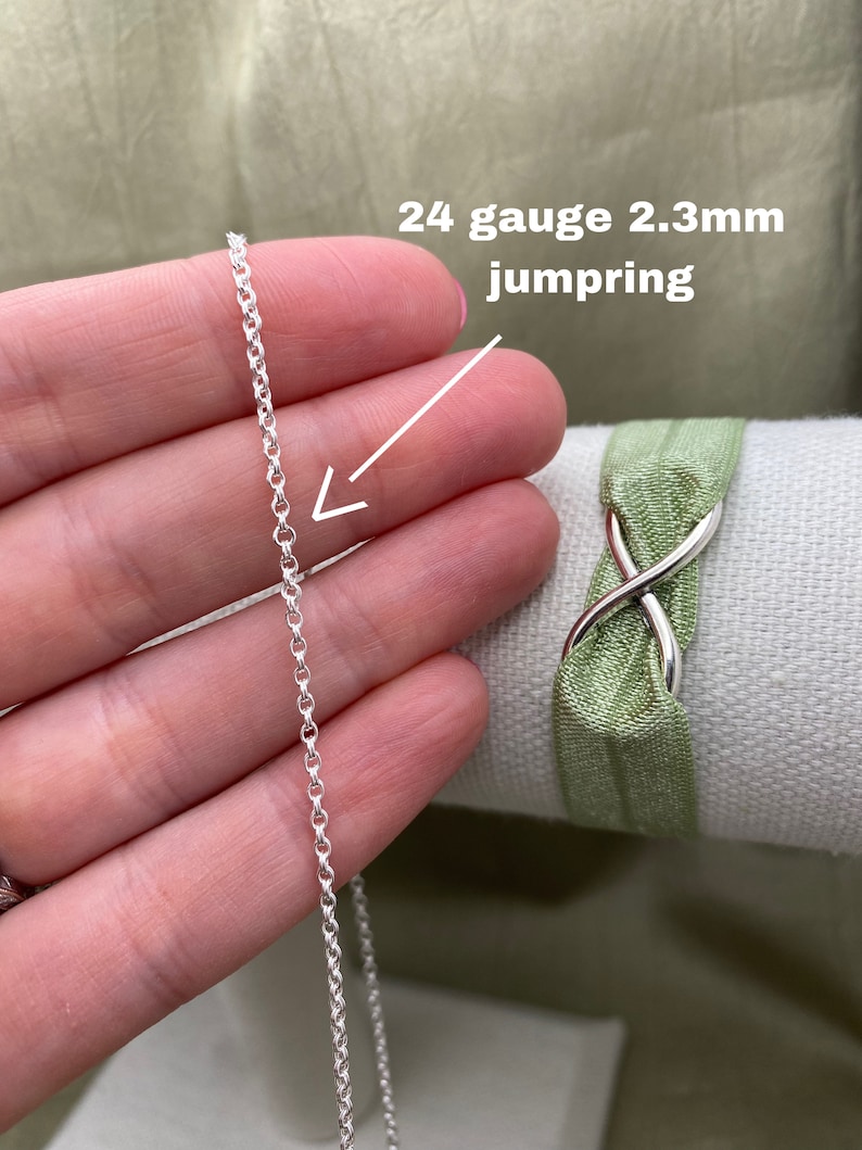 May include: A silver 24 gauge 2.3mm jump ring, shown in a hand holding the ring. The ring is a simple, round shape.