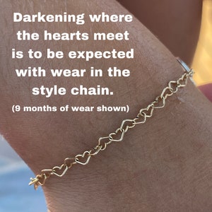 May include: A gold heart-shaped chain bracelet on a person's wrist. The text "Darkening where the hearts meet is to be expected with wear in the style chain. (9 months of wear shown)" is visible on the image.