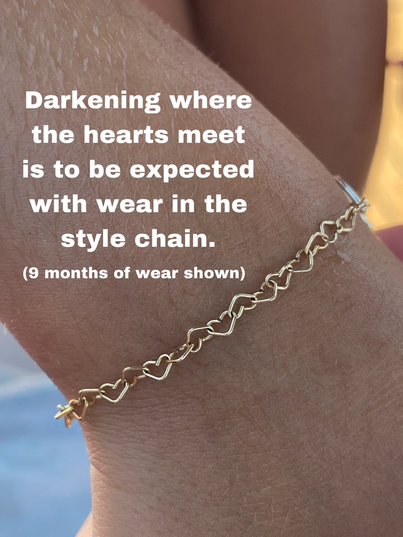 May include: A gold heart-shaped chain bracelet on a person's wrist. The text "Darkening where the hearts meet is to be expected with wear in the style chain. (9 months of wear shown)" is visible on the image.