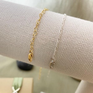 May include: Two delicate chain bracelets, one with a heart-shaped link in gold and the other with a simple chain link in silver.