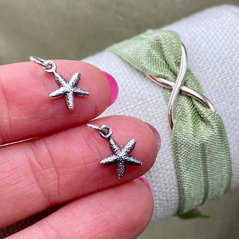 May include: Two silver starfish charms with a textured finish. The charms are hanging from a loop and are perfect for adding a touch of nautical charm to jewelry or crafts.
