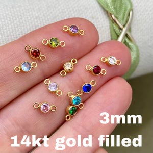 May include: A collection of 14kt gold filled connectors, each featuring a 3mm gemstone in various colors. The gemstones include red, blue, green, pink, purple, and clear. The connectors have a small loop on each end.