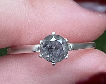 May include: A silver ring with a grey, faceted gemstone set in a prong setting.