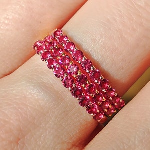 Może przedstawiać: Złoty pierścionek z trzema rzędami czerwonych kamieni szlachetnych. Pierścionek jest noszony na palcu.