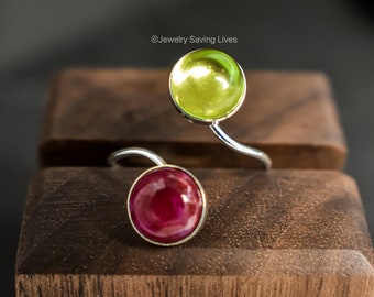 Può includere: Un anello d'argento con due pietre rotonde. La pietra superiore è di colore verde chiaro e la pietra inferiore è di colore rosso scuro. ©Jewelry Saving Lives