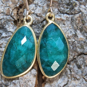 May include: A pair of emerald green gemstone earrings with gold settings. The earrings are teardrop shaped and have a faceted finish.