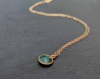 May include: A delicate gold chain necklace with a small, round, dark green gemstone pendant.
