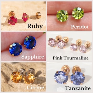 Pode incluir: Um conjunto de 10 pares de brincos de pressão de ouro com pedras preciosas de diferentes cores. As pedras preciosas são rubi, peridoto, safira, turmalina rosa, citrino e tanzanita.