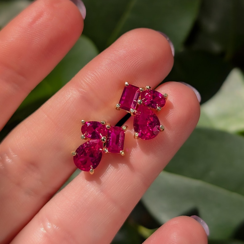 Peut inclure: Une paire de boucles d'oreilles dor&eacute;es orn&eacute;es de grappes de pierres pr&eacute;cieuses rouge rubis vives, de formes rectangulaires et en goutte. Les boucles d'oreilles sont serties de petits accents scintillants, cr&eacute;ant un design luxueux et attrayant.