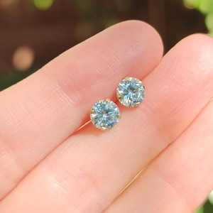 May include: A pair of gold stud earrings with round, clear blue gemstones.