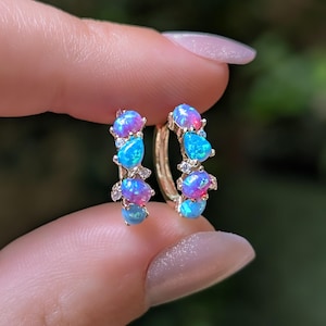 May include: A pair of gold hoop earrings featuring alternating round and teardrop-shaped iridescent opals in shades of blue and pink, accented with small clear stones set along the metal band, creating a vibrant and colorful jewelry piece.