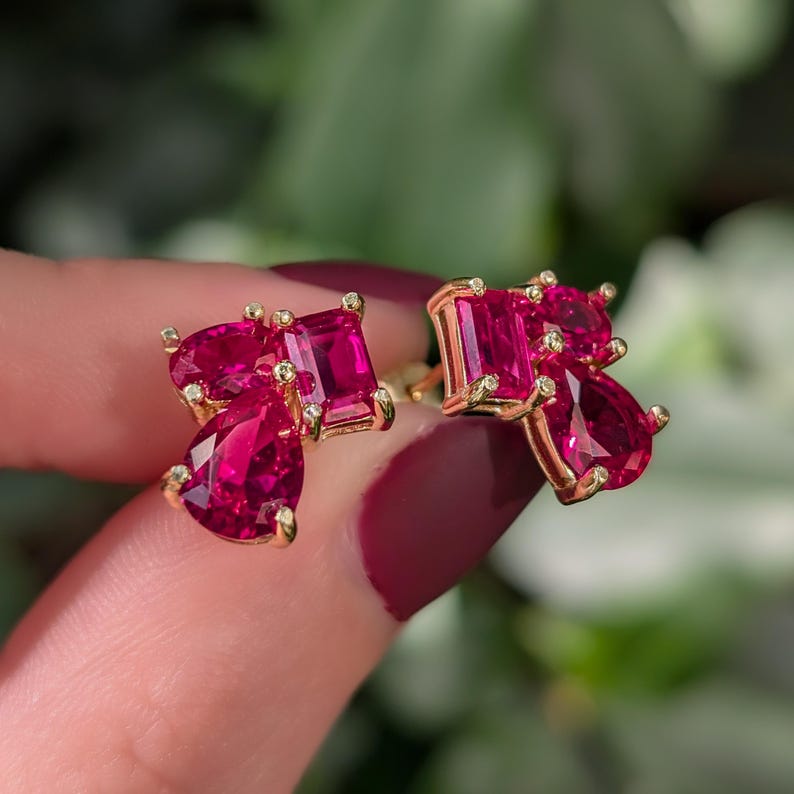 Peut inclure: Une paire de boucles d'oreilles dor&eacute;es orn&eacute;es de pierres pr&eacute;cieuses rouges vives. Chaque boucle d'oreille pr&eacute;sente une combinaison de pierres rectangulaires et en forme de poire, cr&eacute;ant un look unique et accrocheur. Les boucles d'oreilles sont serties dans un m&eacute;tal dor&eacute;.