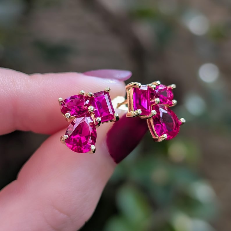 Peut inclure: Une paire de boucles d'oreilles &agrave; clous dor&eacute;es, chacune orn&eacute;e d'un groupe de pierres pr&eacute;cieuses fuchsia vives de diff&eacute;rentes formes. Les pierres pr&eacute;cieuses comprennent des tailles poire, c&oelig;ur et rectangulaires, cr&eacute;ant un affichage &eacute;blouissant de couleur et de lumi&egrave;re.