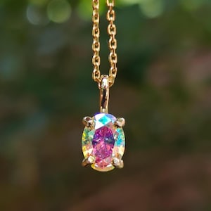 May include: A gold-toned chain necklace featuring an oval-shaped pendant with a faceted, iridescent stone that displays shifting colors including pink, purple, and yellow. The stone is held in a four-prong setting attached to a delicate metal link chain.
