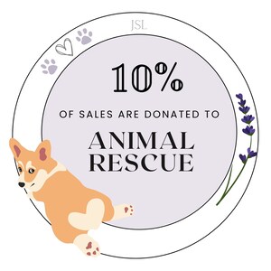 Puede incluir: Un c&iacute;rculo morado y blanco con el texto "JSL" en la parte superior, "10% de las ventas se donan a ANIMAL RESCUE" en el centro, y un dise&ntilde;o de huella de pata, coraz&oacute;n y flor de lavanda alrededor del borde. Un perro corgi de dibujos animados est&aacute; acurrucado en la parte inferior izquierda del c&iacute;rculo.