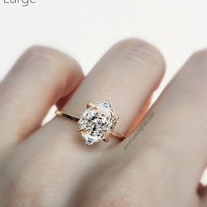 May include: A gold ring with a clear, faceted, geometric gemstone. The ring is on a person's finger. The text "jewelry saving lives.com" is visible in the image.