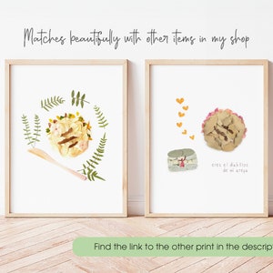 May include: Two framed prints with pressed flower art. The first print features a yellow and brown arepa with green leaves around it. The second print features a pink arepa with a yellow heart above it and the text "eres el dieblitos de mi arepe".