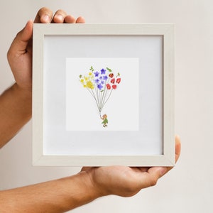 May include: A white frame with a white mat holds a print of a small person holding a string of colorful flowers. The flowers are yellow, blue, and red.