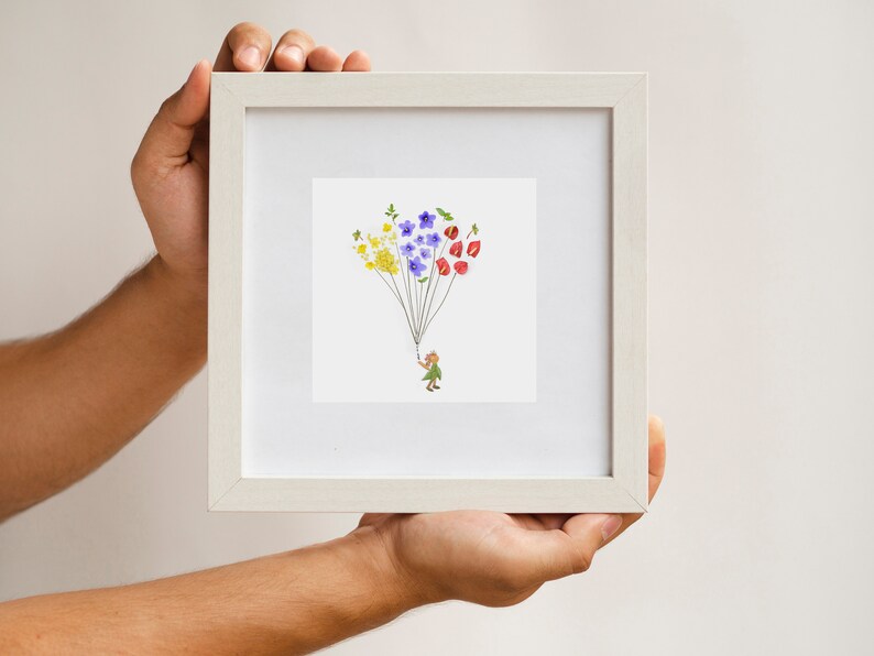May include: A white frame with a white mat holds a print of a small person holding a string of colorful flowers. The flowers are yellow, blue, and red.