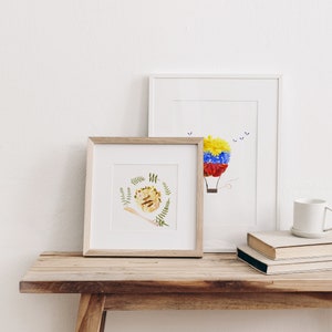 May include: Two framed floral art prints on a wooden table. The print on the left features a hedgehog made of flowers and leaves. The print on the right features a hot air balloon made of flowers.