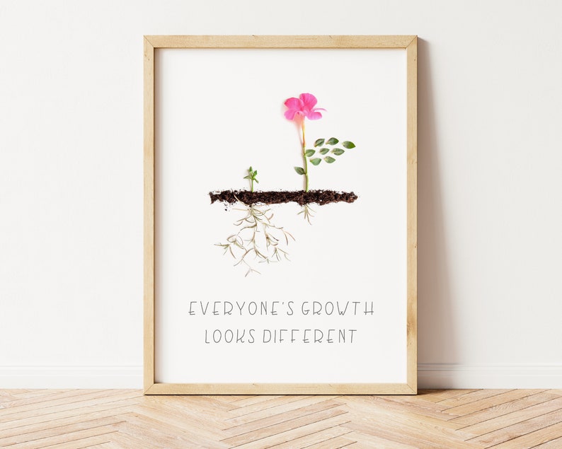 Op de afbeelding: Een ingelijst print met een roze bloem en groene bladeren die groeien uit een bruine lijn die de grond voorstelt. De wortels van de plant zijn zichtbaar onder de grondlijn. De tekst "EVERYONE'S GROWTH LOOKS DIFFERENT" is onder de afbeelding gedrukt.