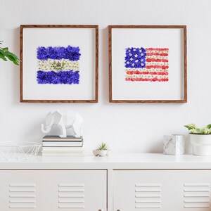 May include: Two framed floral art prints depicting the flags of El Salvador and the United States. The flags are made of colorful flower petals.