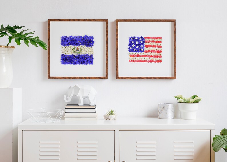 May include: Two framed floral art prints depicting the flags of El Salvador and the United States. The flags are made of colorful flower petals.