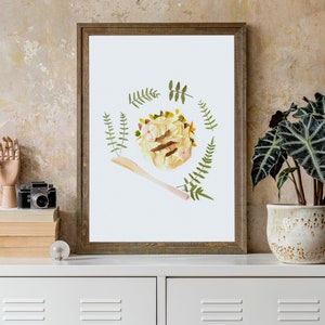 May include: A framed print of a floral arrangement depicting a bowl of pasta with a wooden spoon. The arrangement is surrounded by green leaves and flowers.