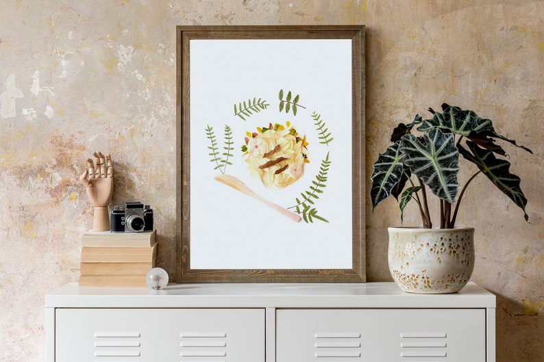 May include: A framed print of a floral arrangement depicting a bowl of pasta with a wooden spoon. The arrangement is surrounded by green leaves and flowers.