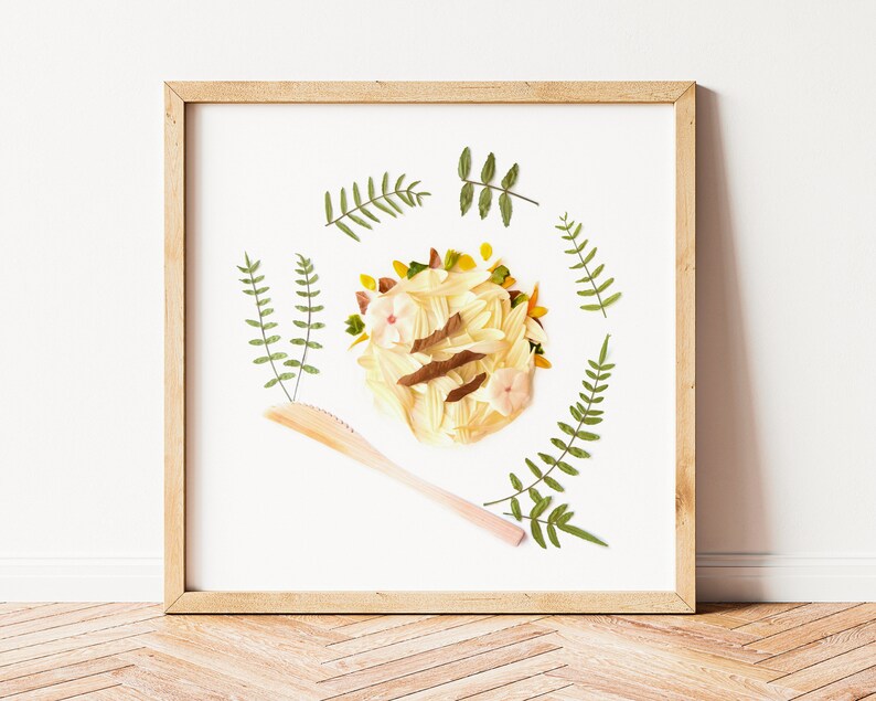 May include: A framed artwork featuring a circular arrangement of dried flowers and leaves in shades of green, yellow, and pink. A wooden stick is placed diagonally across the artwork.